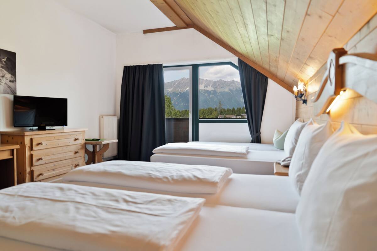 A hotel room with two beds, a TV, a dresser, and a view of mountains through a large window.