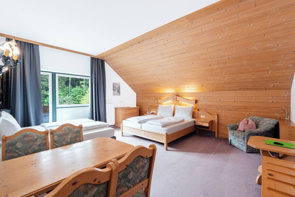 A room with a wooden ceiling, a bed, a desk, a chair, and a table.