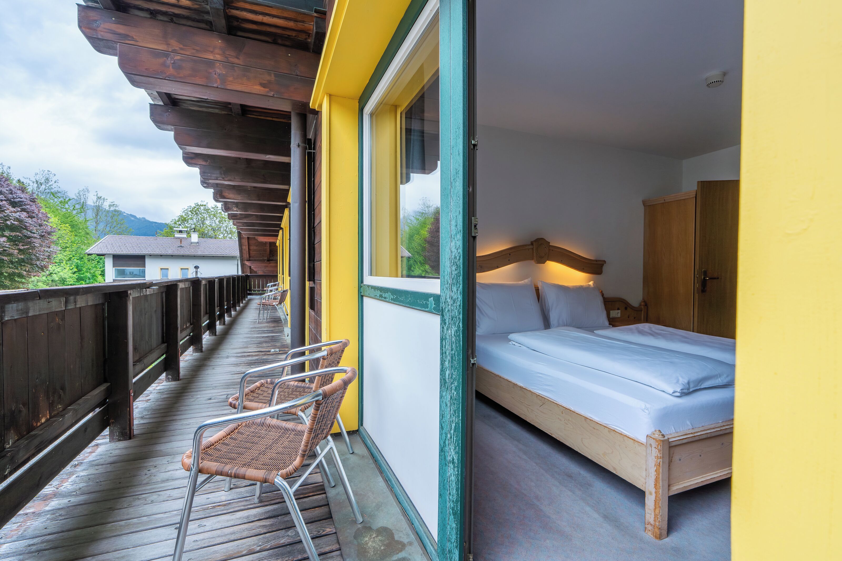 Una terraza de madera con sillas de mimbre, una cama con colchón blanco y vistas a la montaña.