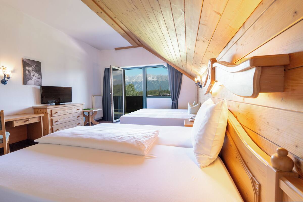 A hotel room with two beds, a desk, a television, and a view of mountains through a large window.