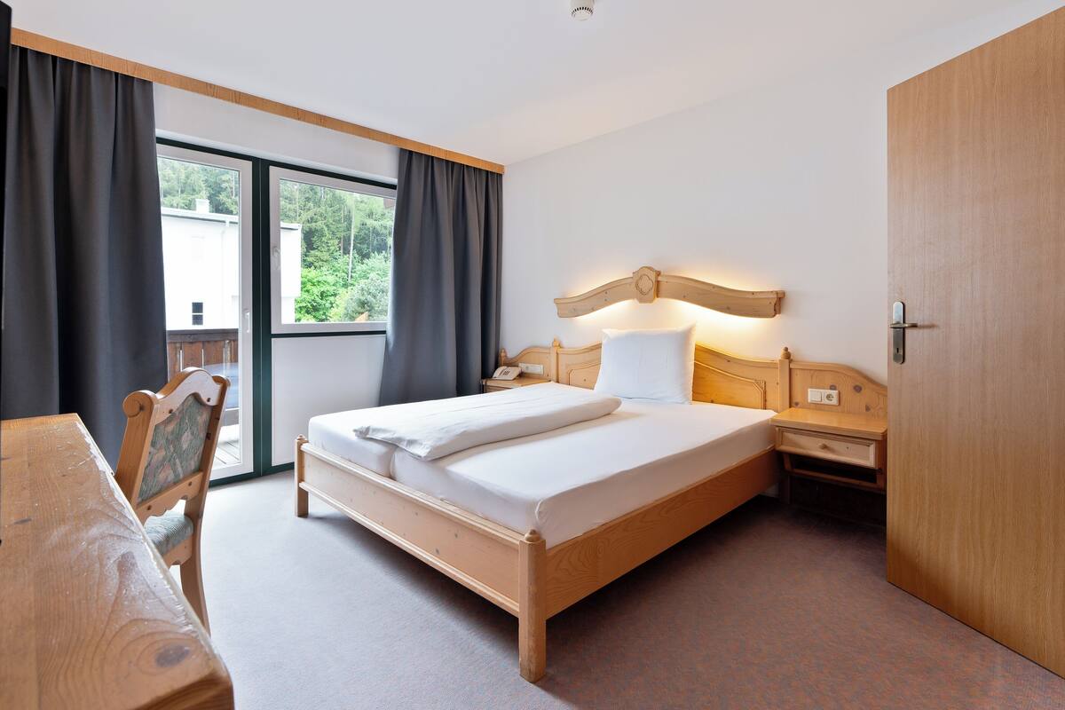 A hotel room with a wooden bed, a desk, a chair, a nightstand, and a wardrobe.