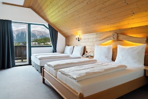 Habitación con tres camas, techo de madera, ventanas amplias y vistas a la montaña.