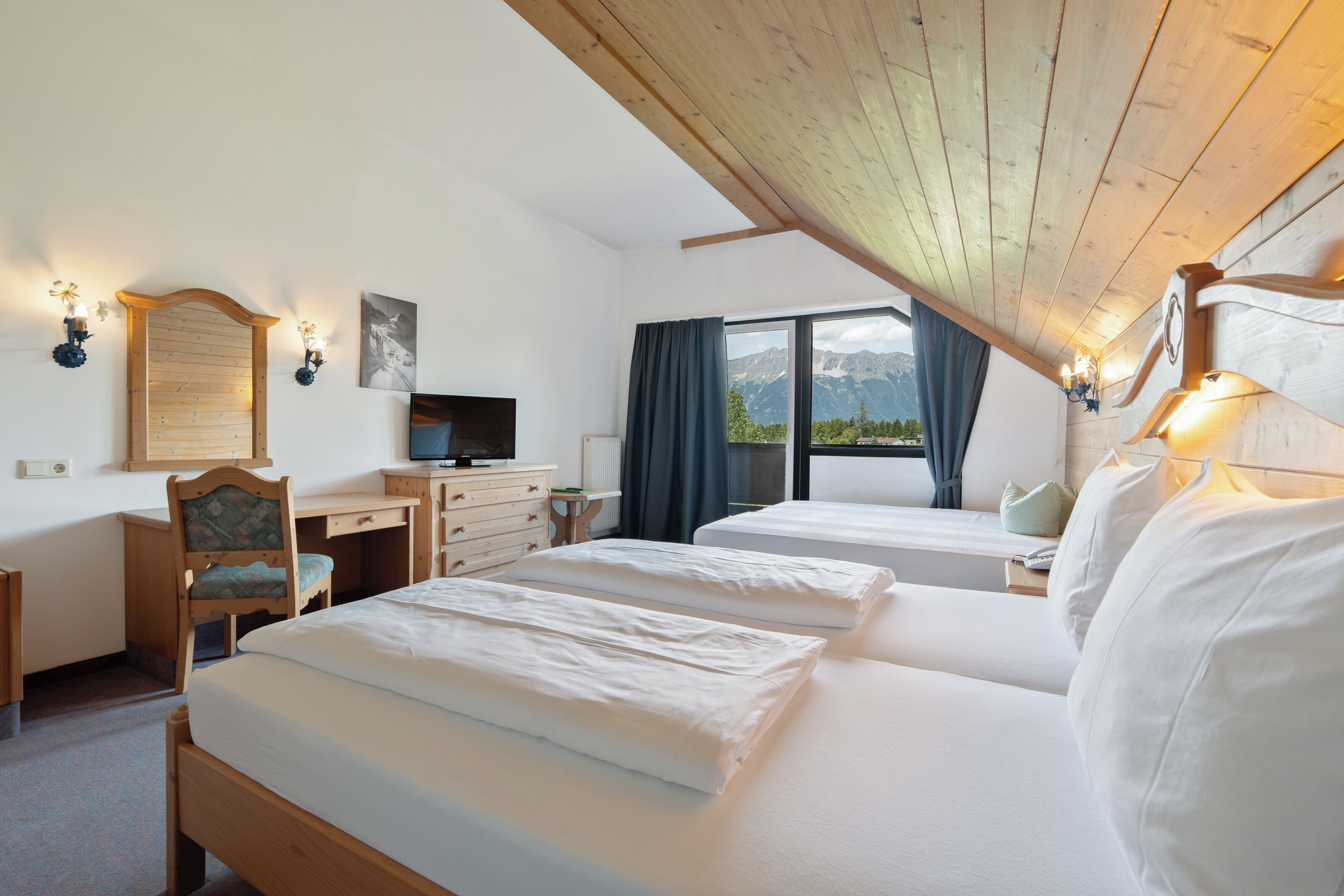 Une chambre d’hôtel avec deux lits, un bureau, une chaise, une télévision et une fenêtre donnant sur la montagne.