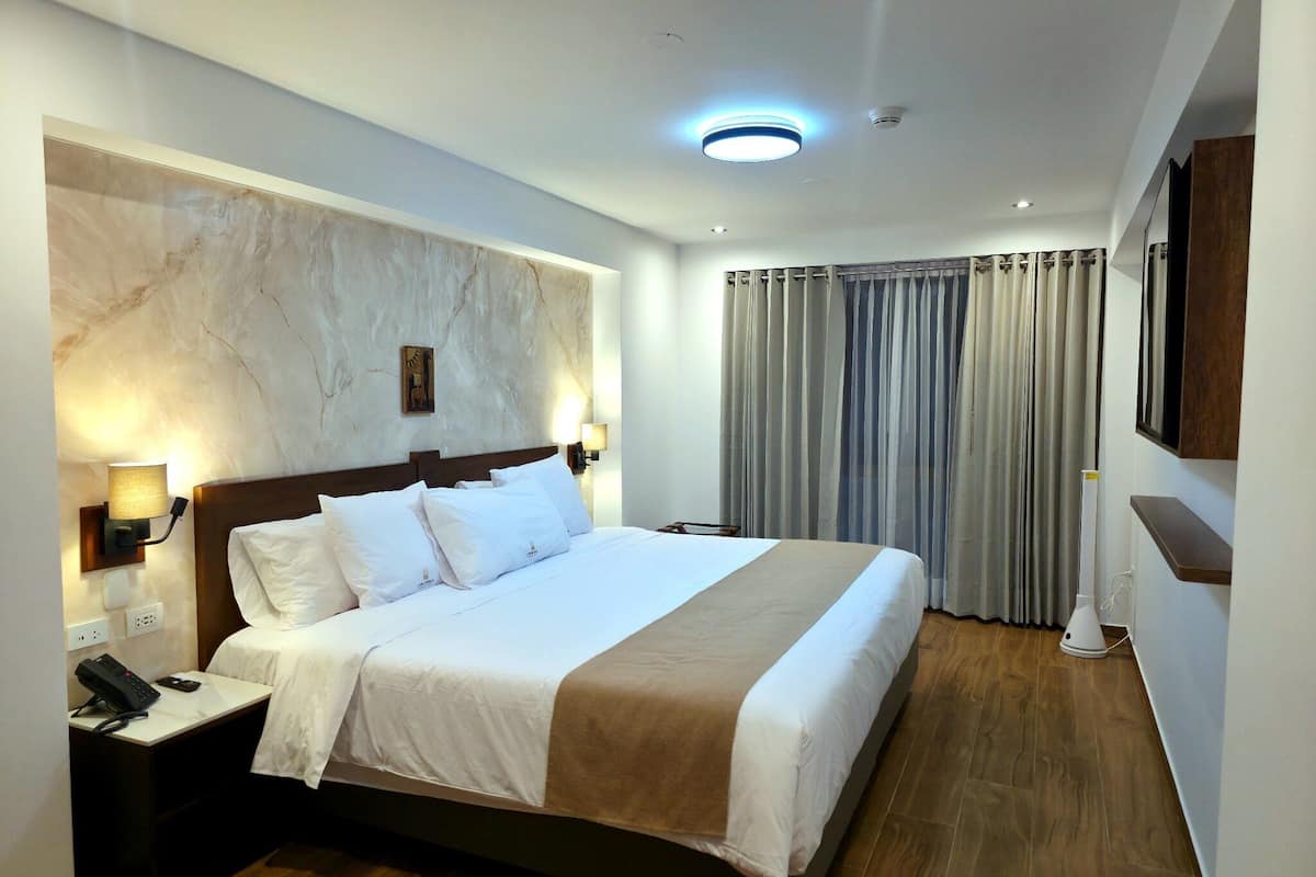 Habitació d'hotel amb llit, taulell de nit, làmpada i televisió penjada.