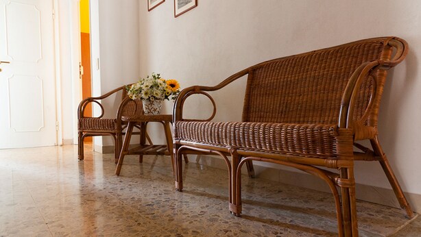 Una habitación con un sofá de mimbre, un sillón a juego y una mesita con un jarrón de flores.