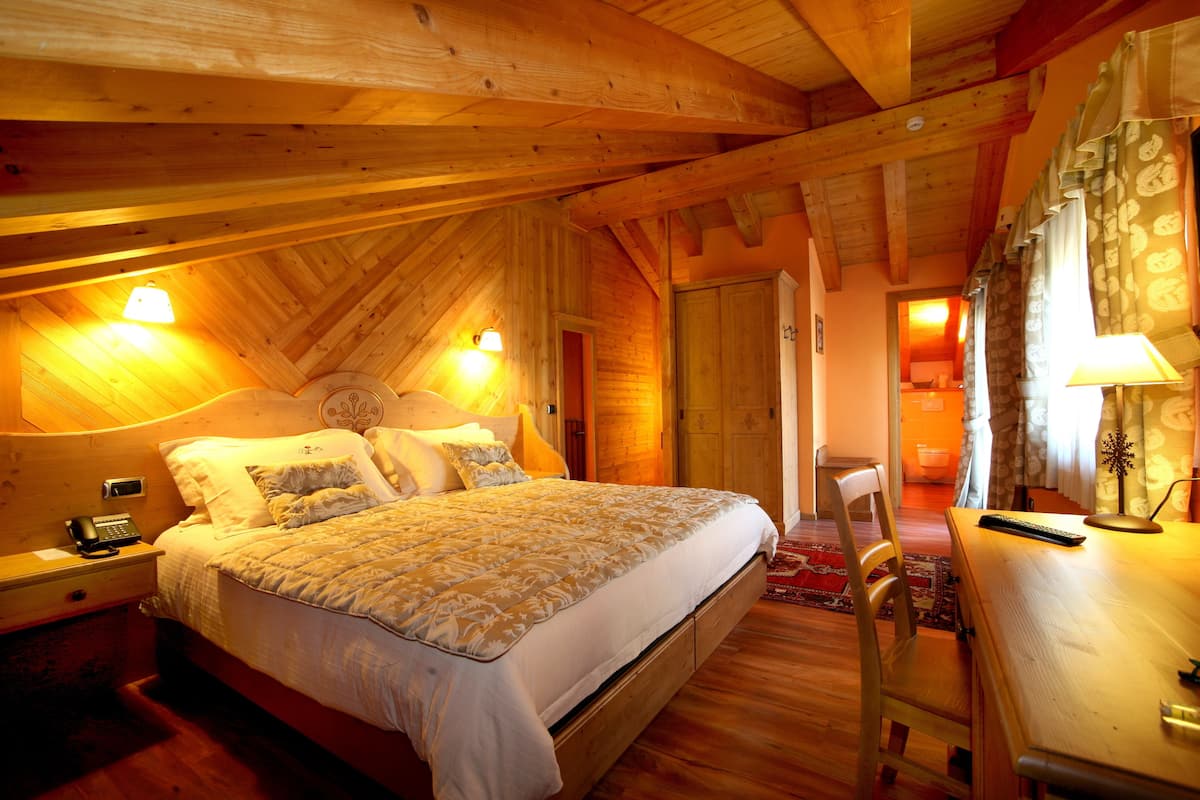 A cozy bedroom with a wooden ceiling, a bed with a patterned bedspread, bedside lamps, and a desk with a lamp.