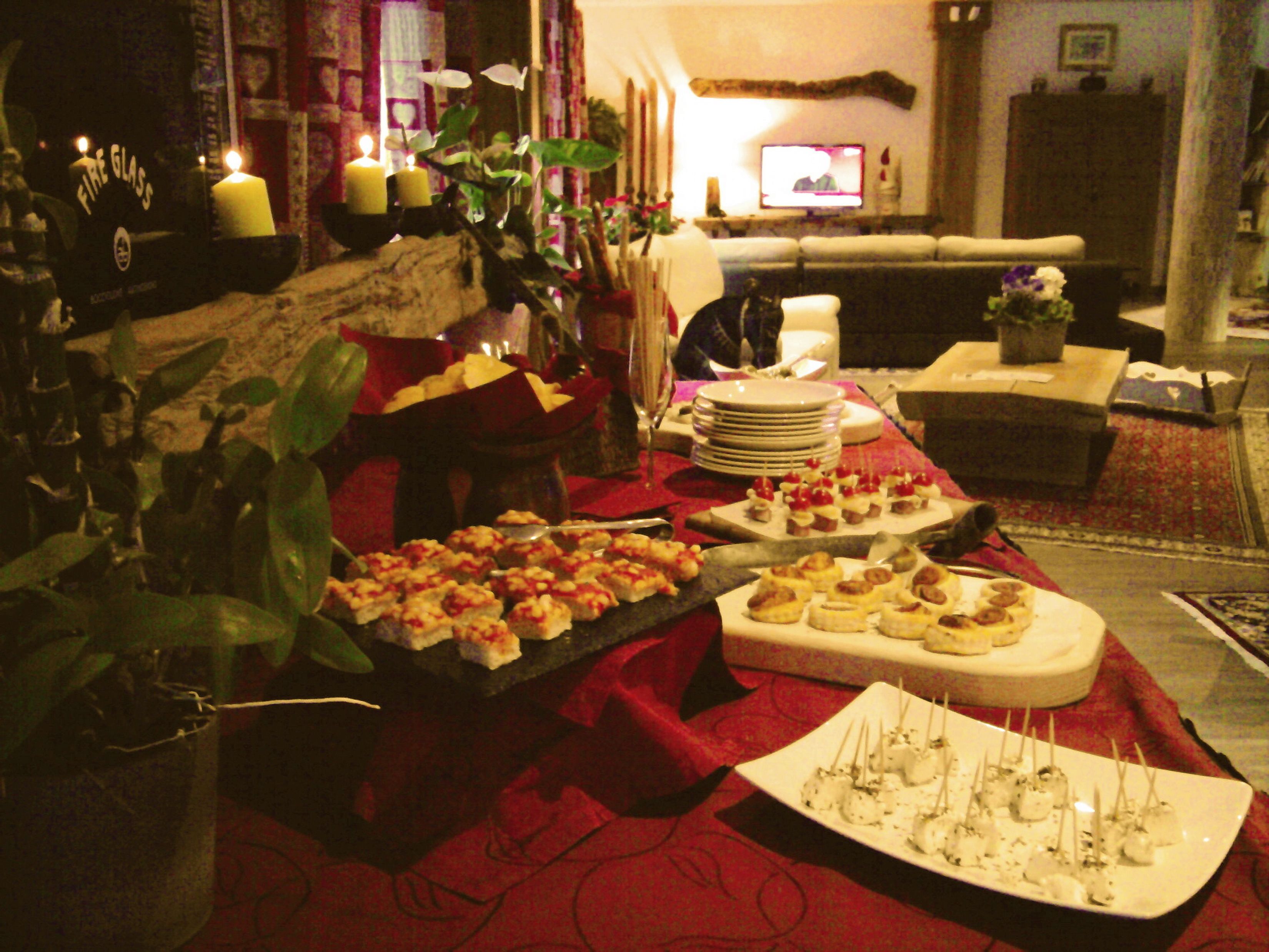 Un comedor con una mesa de buffet dispuesta con varios aperitivos, un televisor al fondo y una disposición de asientos acogedora.