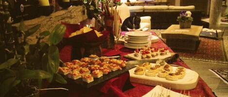 Un comedor con una mesa de buffet dispuesta con varios aperitivos, un televisor al fondo y una disposición de asientos acogedora.
