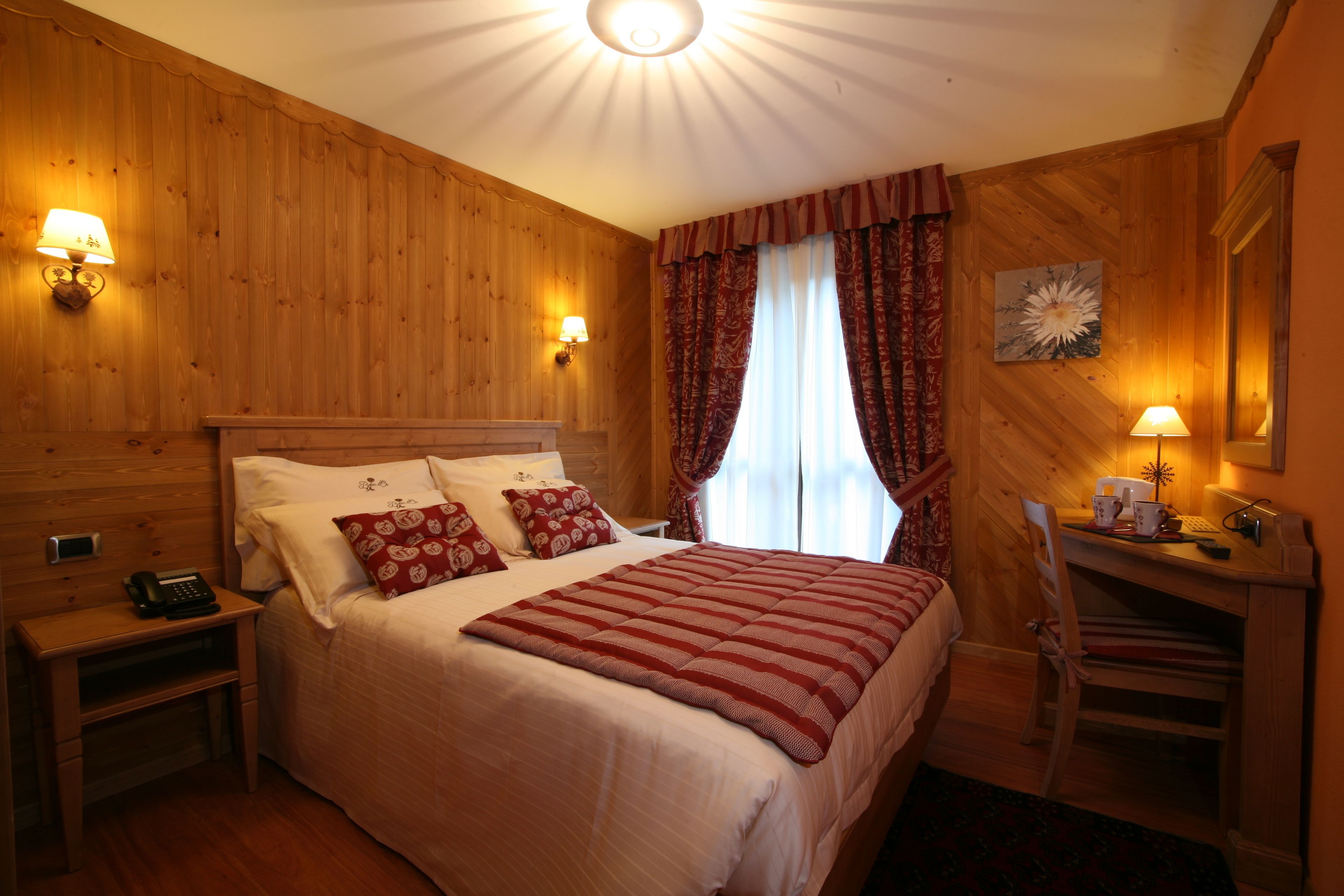 A wooden-paneled room with a bed, bedside lamps, a desk, and a chair.