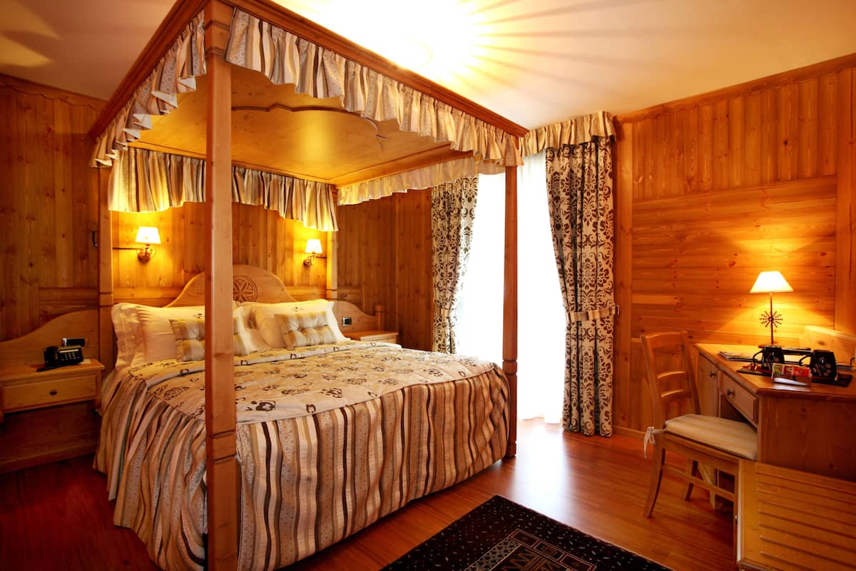 A four-poster bed with a canopy, a wooden desk with a chair, and a nightstand with a lamp.