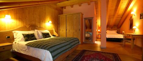 Un dormitorio acogedor con techo de madera, una cama grande con colcha verde y blanca, un tapete estampado en rojo y azul, y un armario de madera.