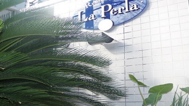 A sign for "La Perla" with a grid-patterned wall and a large potted plant in the foreground. - Flat Residencial La Perla (Fortaleza)