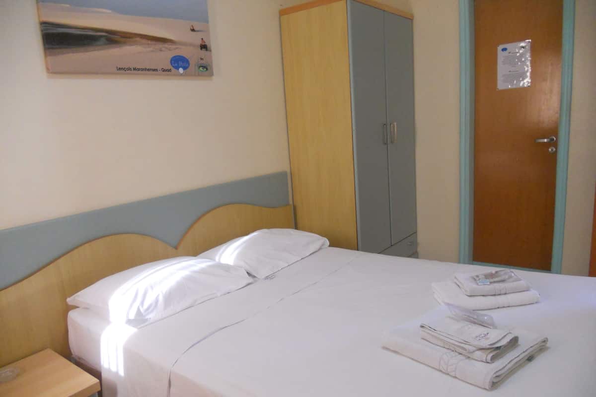 Una habitación de hotel con cama, armario, mesita de noche y un cartel en la pared.