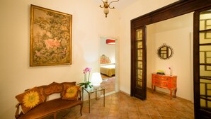 Una habitación con un banco de madera, una mesita con una lámpara, un cuadro en la pared y un aparador con un espejo.