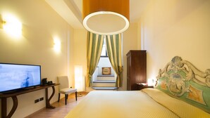 Habitación de hotel con una cama grande, un televisor sobre un soporte de madera, una silla, un escritorio y una escalera que lleva a un piso superior.