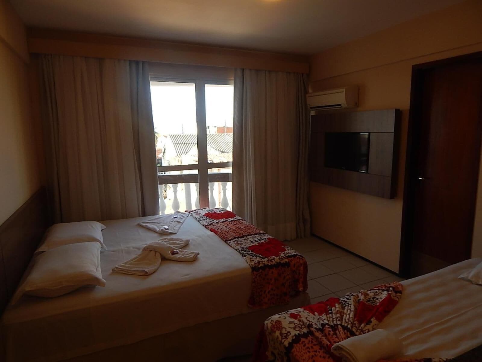 Une chambre d’hôtel avec deux lits, un téléviseur fixé au mur et un balcon avec des rideaux.