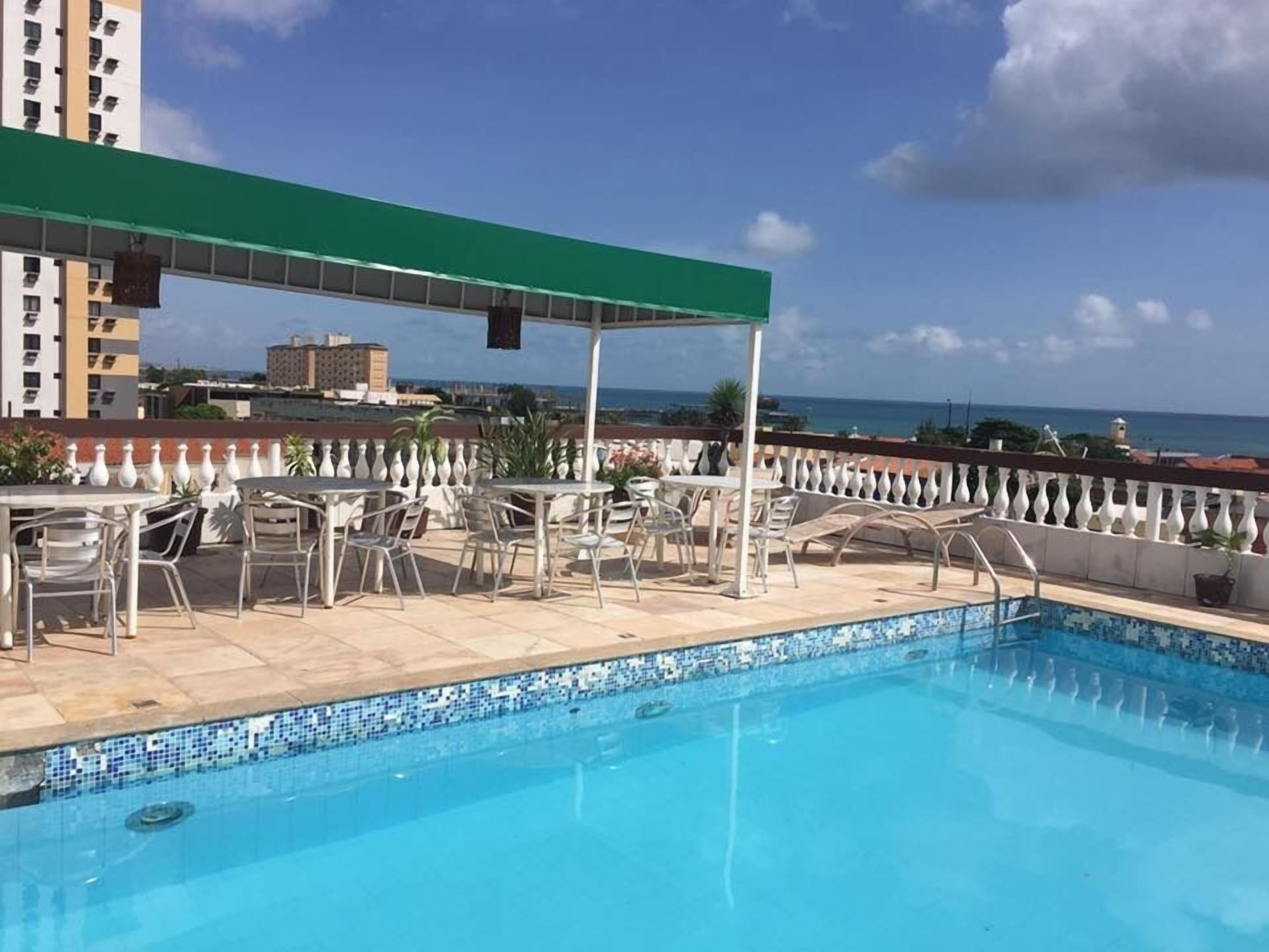 A rooftop pool area with a view of the ocean, surrounded by outdoor seating and a covered patio.