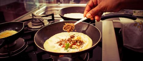 A hand sprinkling seasoning over a pancake in a frying pan on a stove.