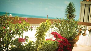 A balcony with potted plants and flowers, overlooking a beach and ocean. - Algarve Praia Hotel (Fortaleza)