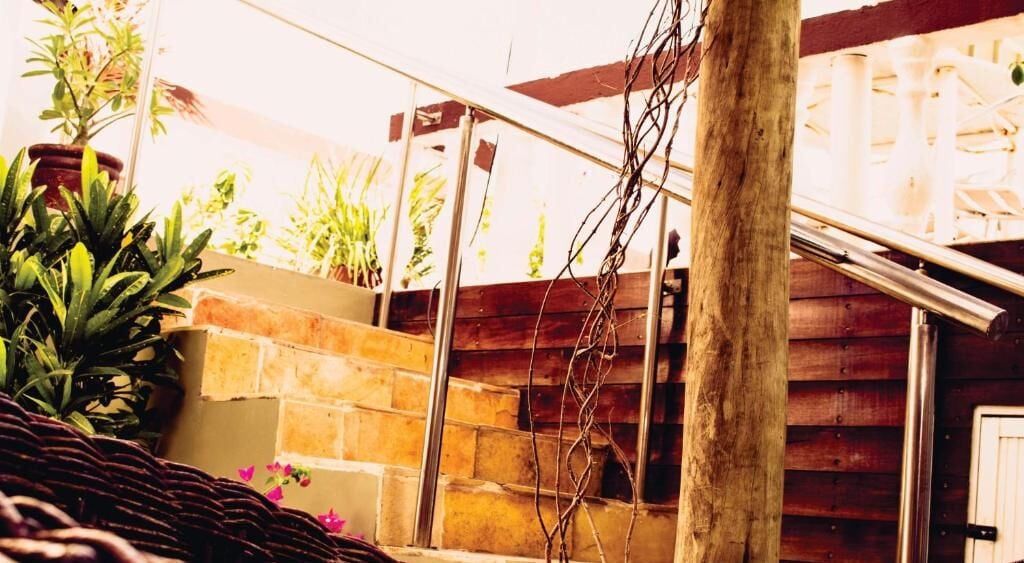 A wooden staircase leading to a covered outdoor area with potted plants and a brick wall.