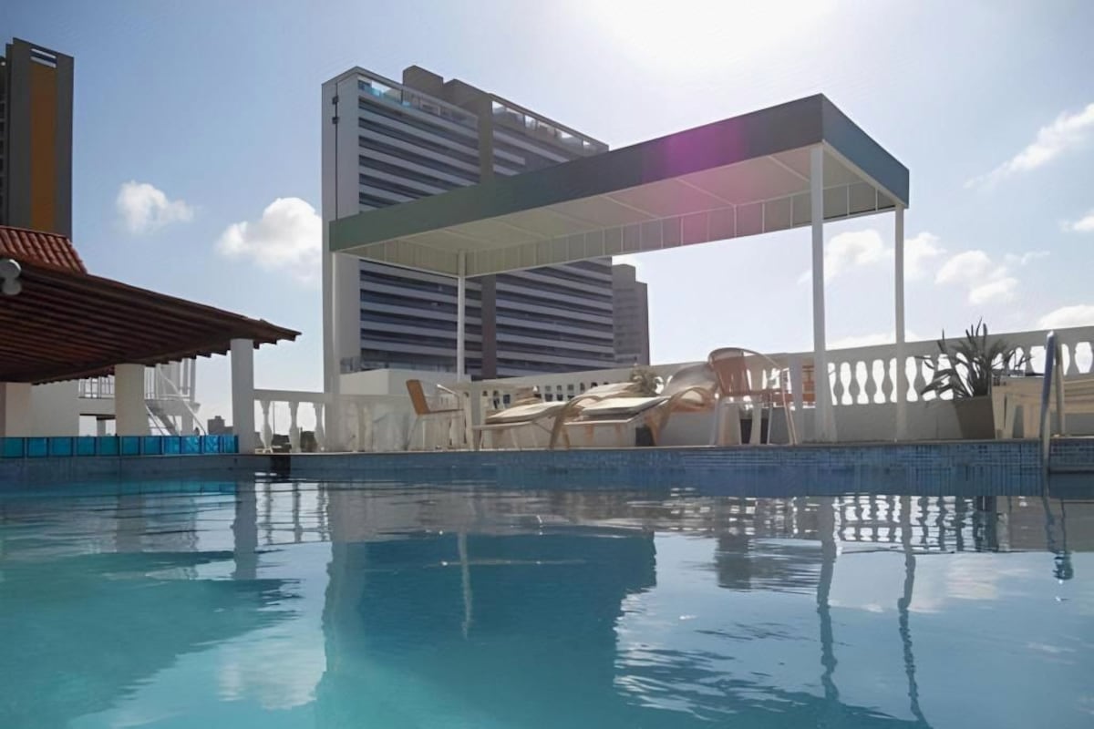 A swimming pool with a covered area, adjacent buildings, and a clear sky.