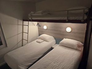 Habitación con literas, dos camas, una escalera y dos lámparas fijadas a la pared.