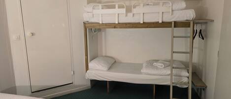 A bunk bed room with a door, a small table, and a pair of scissors on the wall.