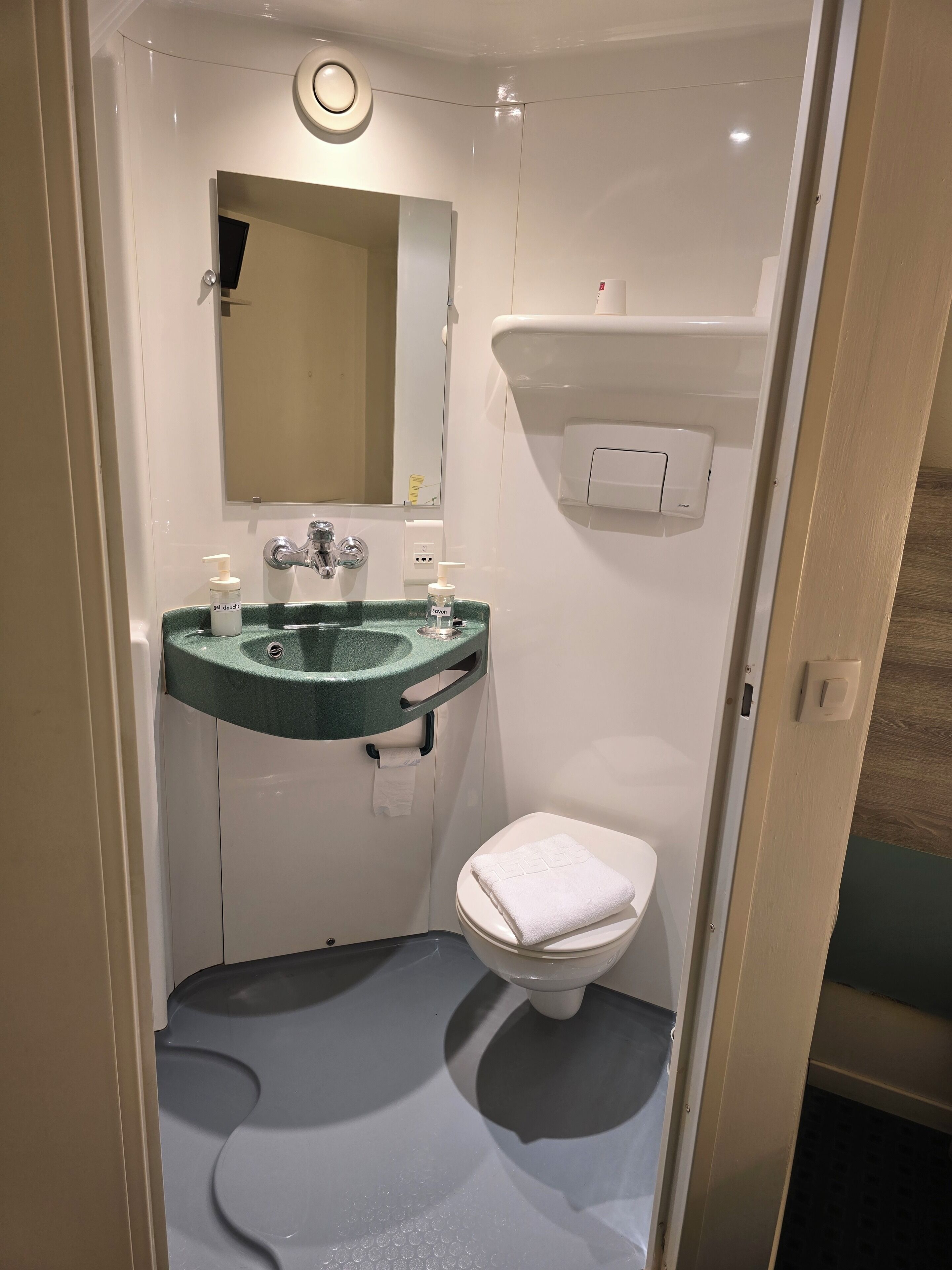Un baño pequeño con un lavamanos verde, inodoro y espejo.