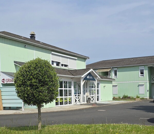 Un hotel con fachada verde, un pequeño árbol en la entrada y un cartel que dice 'BRIT HOTEL'.
