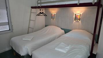 Habitación con dos camas individuales, una litera encima, ventana con persianas, perchero y luces fijadas a la pared.