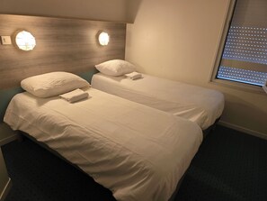 A hotel room with two beds, each with white linens and pillows, a wooden headboard, and wall-mounted lights.