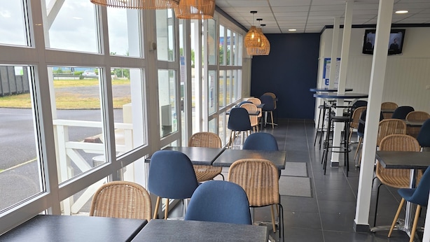 A restaurant with large windows, wicker chairs, and tables. - Brit Hotel Essentiel Poitiers – Gare du Futuroscope (Jaunay-Marigny)