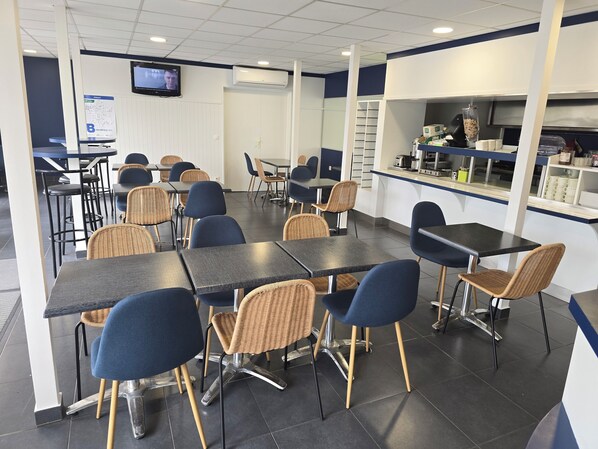 A restaurant with tables and chairs, a television screen, and a kitchen area.