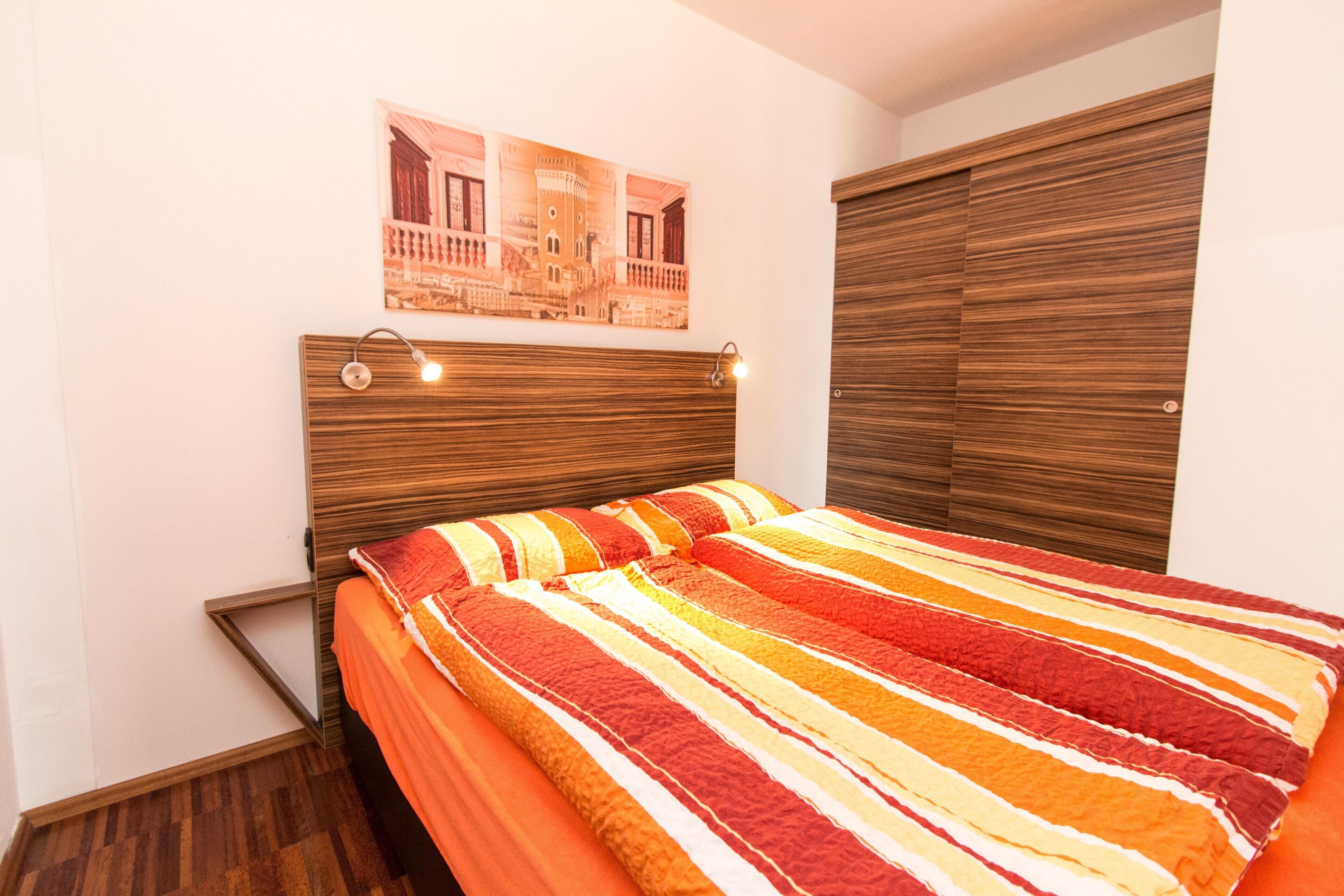 A bedroom with a bed, a wooden headboard, a wall-mounted light fixture, and a framed picture above the bed.