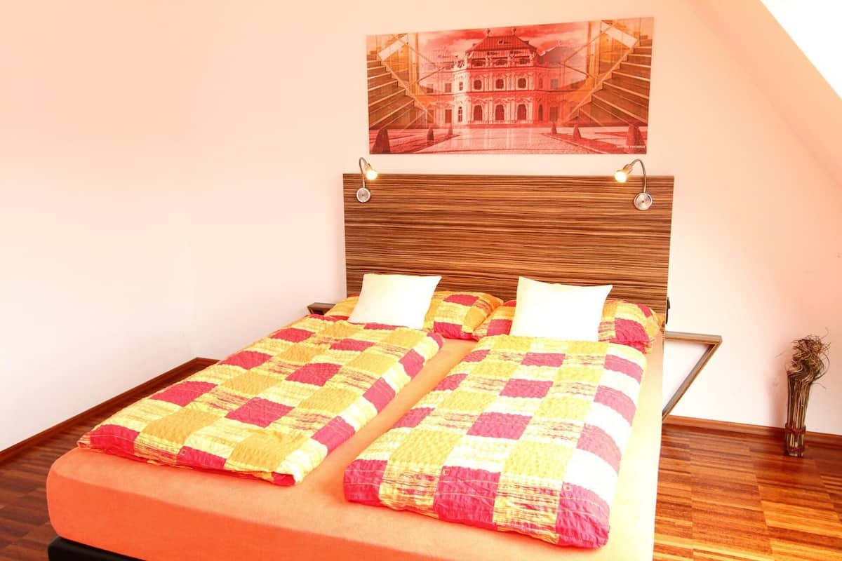Uma cama de casal com cabeceira de madeira, duas almofadas e um colcha colorida.