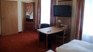 A hotel room with a bed, a desk with a chair, a television, and a door leading to another room. - Hotel-Gasthof-Fellner (Furth im Wald)