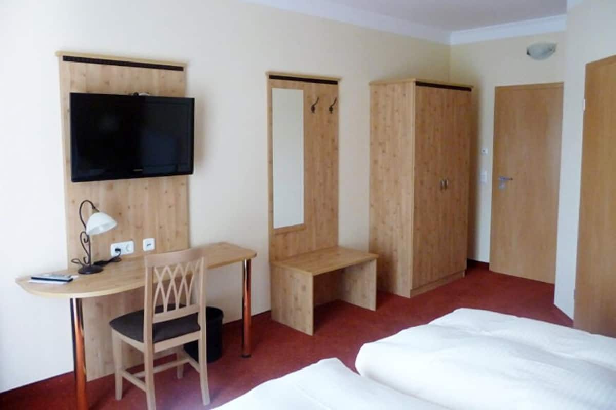 Ein Hotelzimmer mit Holzschreibtisch, Fernseher, Kleiderschrank und Bett.