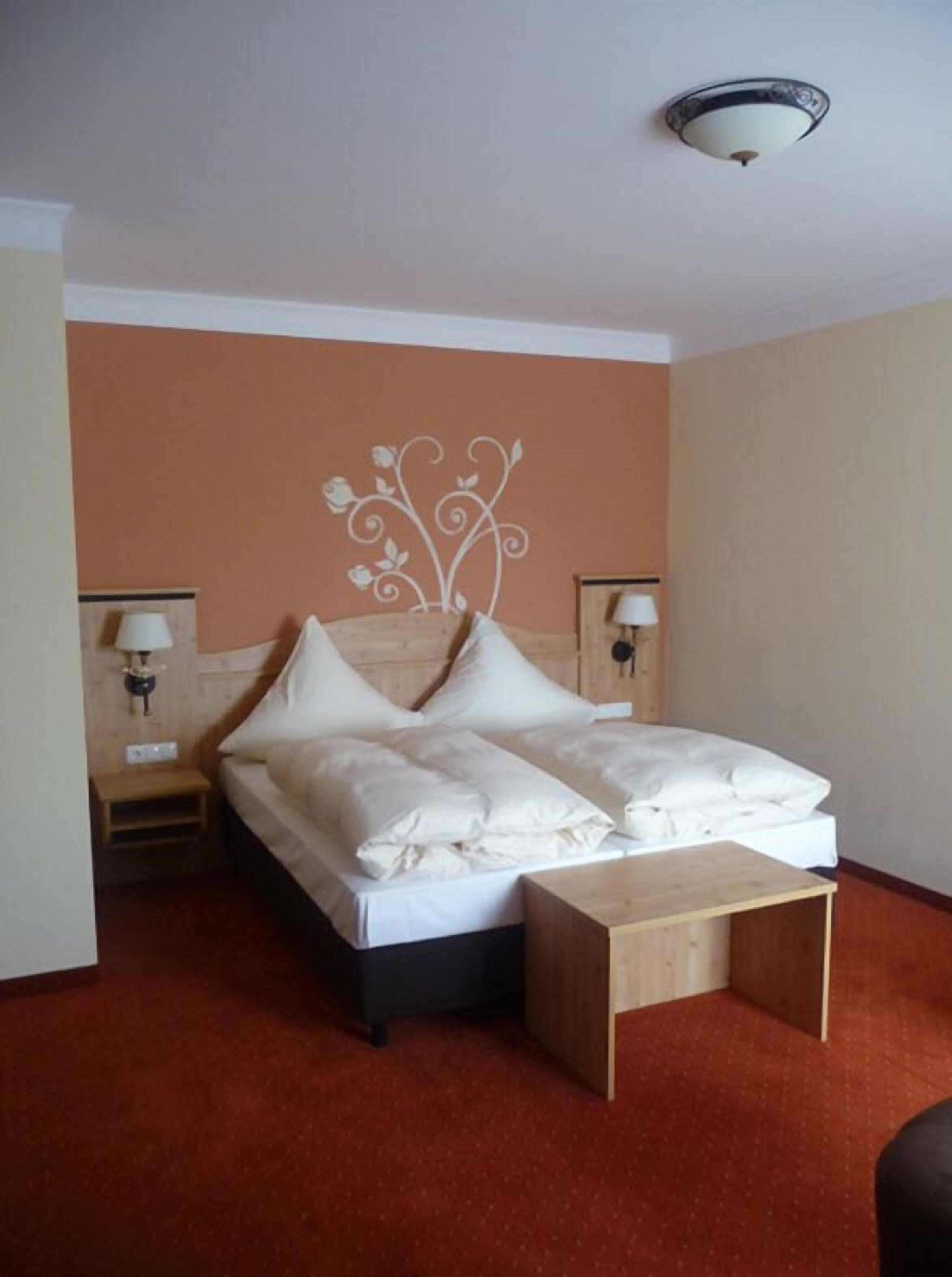 Una habitación de hotel con cama, mesita de noche y lámpara de pared.