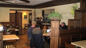 Un interior de restaurante con mobiliario de madera, una mesa central con una planta y una pared con un cartel.