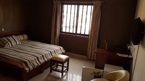 Quarto com cama, escrivaninha, cadeira e janela com cortinas.