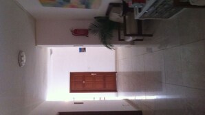 Um corredor estreito com uma porta de madeira no final, uma pequena planta e um quadro na parede.