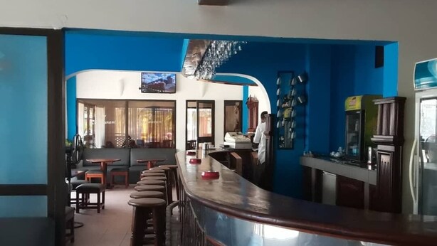 Uma área de bar com balcão curvo, banquetas e uma tela de televisão.