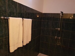 Un baño con paredes de azulejos oscuros, una ducha con cabezal de ducha manual y dos toallas colgadas en un perchero.