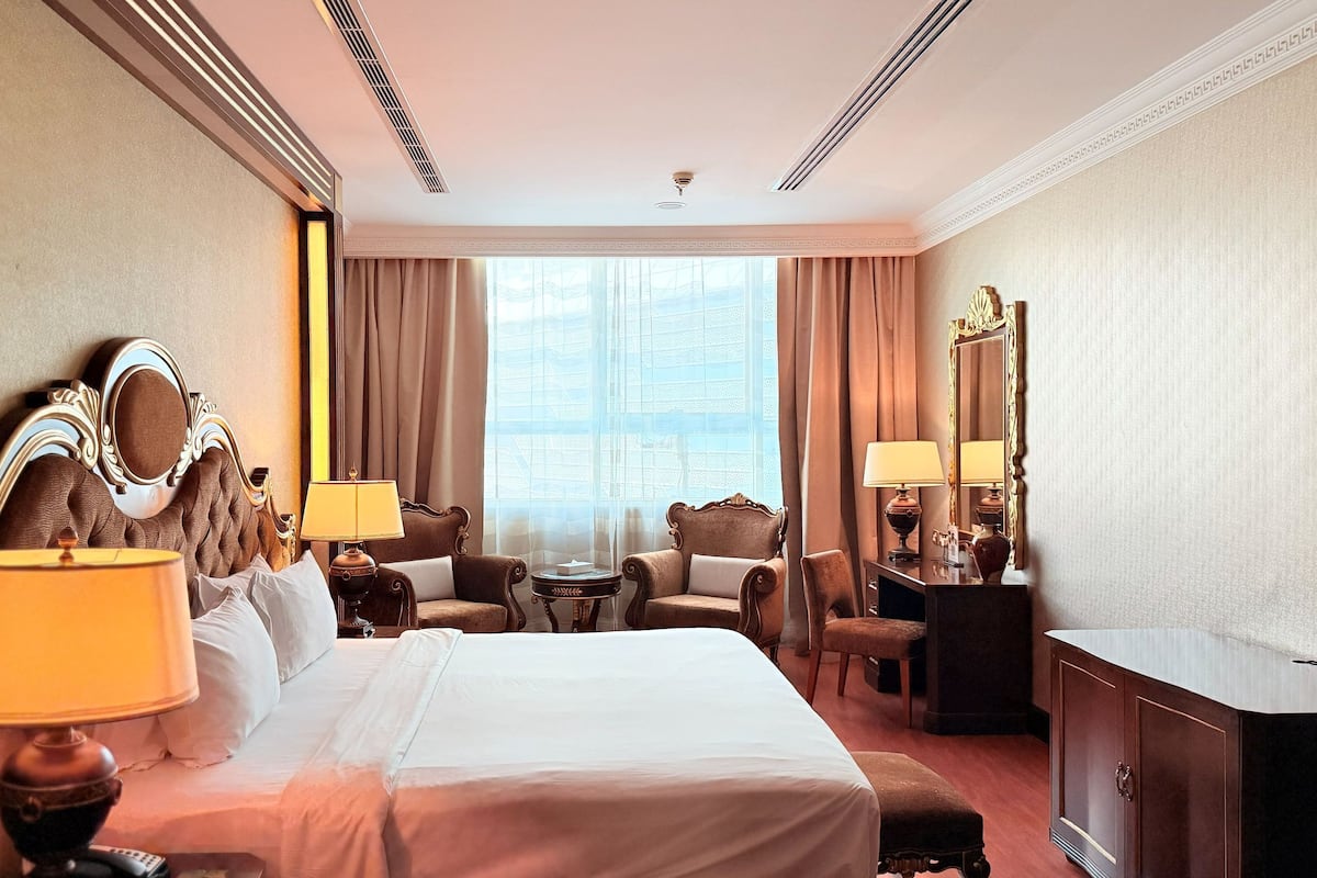 Une chambre d’hôtel avec un grand lit, deux fauteuils, une petite table, un bureau et un grand miroir.