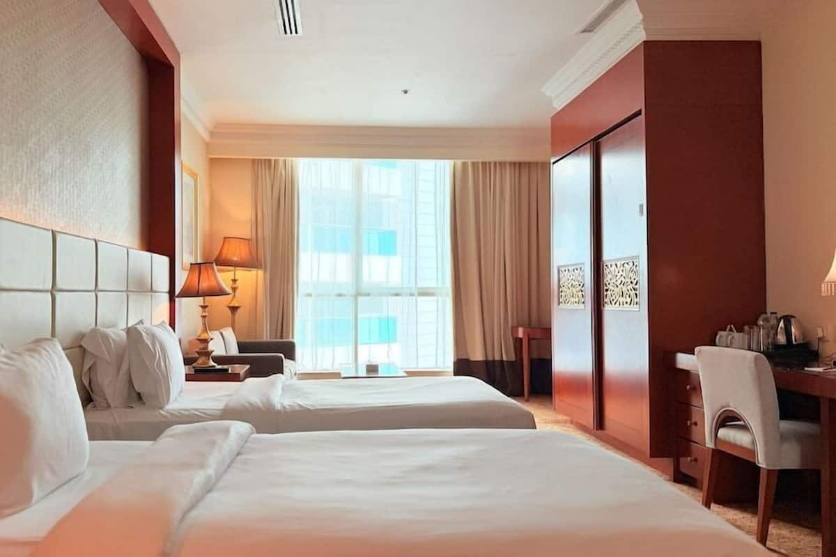 Une chambre d’hôtel avec deux lits, un bureau, une chaise, une lampe et une grande fenêtre.