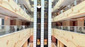 Een meerlaags atrium met glazen balustrades, een centraal lichtarmatuur en een symmetrisch ontwerp.