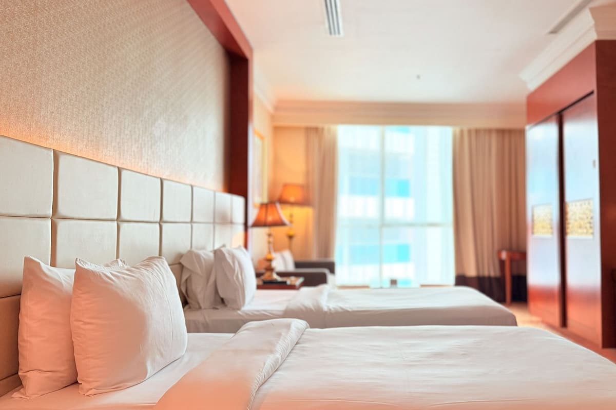Une chambre d’hôtel avec deux lits, un bureau, une chaise et une lampe.