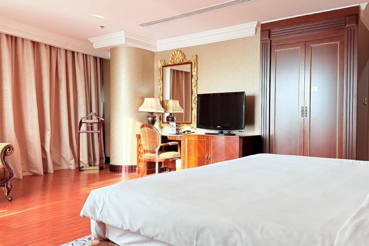 Une chambre d’hôtel avec un grand lit, un bureau avec une télévision, une chaise et une armoire.