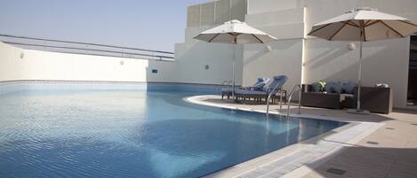 Una piscina al aire libre, sombrillas, sillones reclinables de piscina