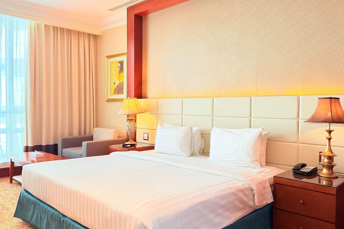 Une chambre d’hôtel avec un grand lit, un bureau, une chaise, une table de chevet avec une lampe et une fenêtre avec des rideaux.